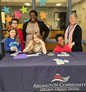 picture of students with librarian and credit union rep seated at a table with a blue tablecloth from the arlington federal credit union