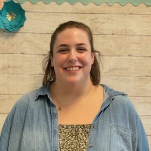 Picture of school social worker CJ Burka smiling and standing front a wall