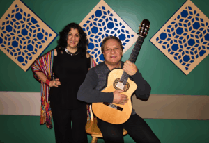 A performing duo, one is seated holding a guitar
